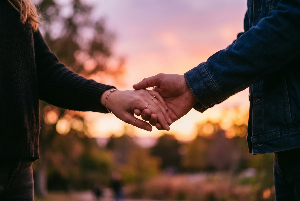 Two people gently holding hands at sunset